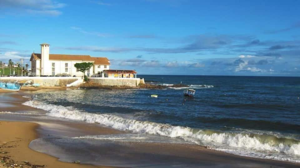 Une plage avec des vagues, un bâtiment et un bateau.