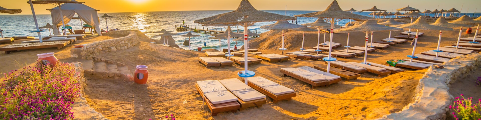 A beach with sun loungers, umbrellas, and a sunset over the ocean.