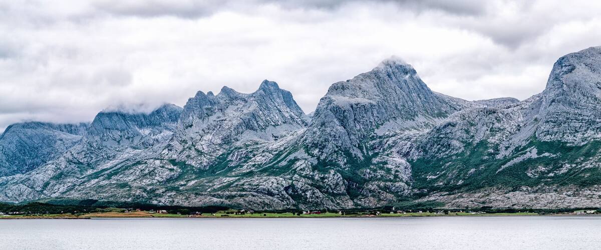 A mountain range with snow-covered peaks and a lake in the foreground.