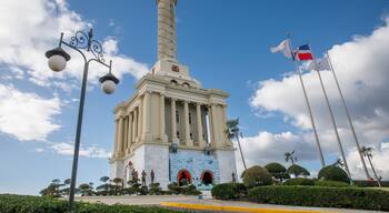 A monument with a tall column and a cross on top, surrounded by statues and flags.