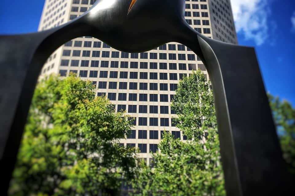 A sculpture of a bird in front of a tall building with a grid pattern of windows.