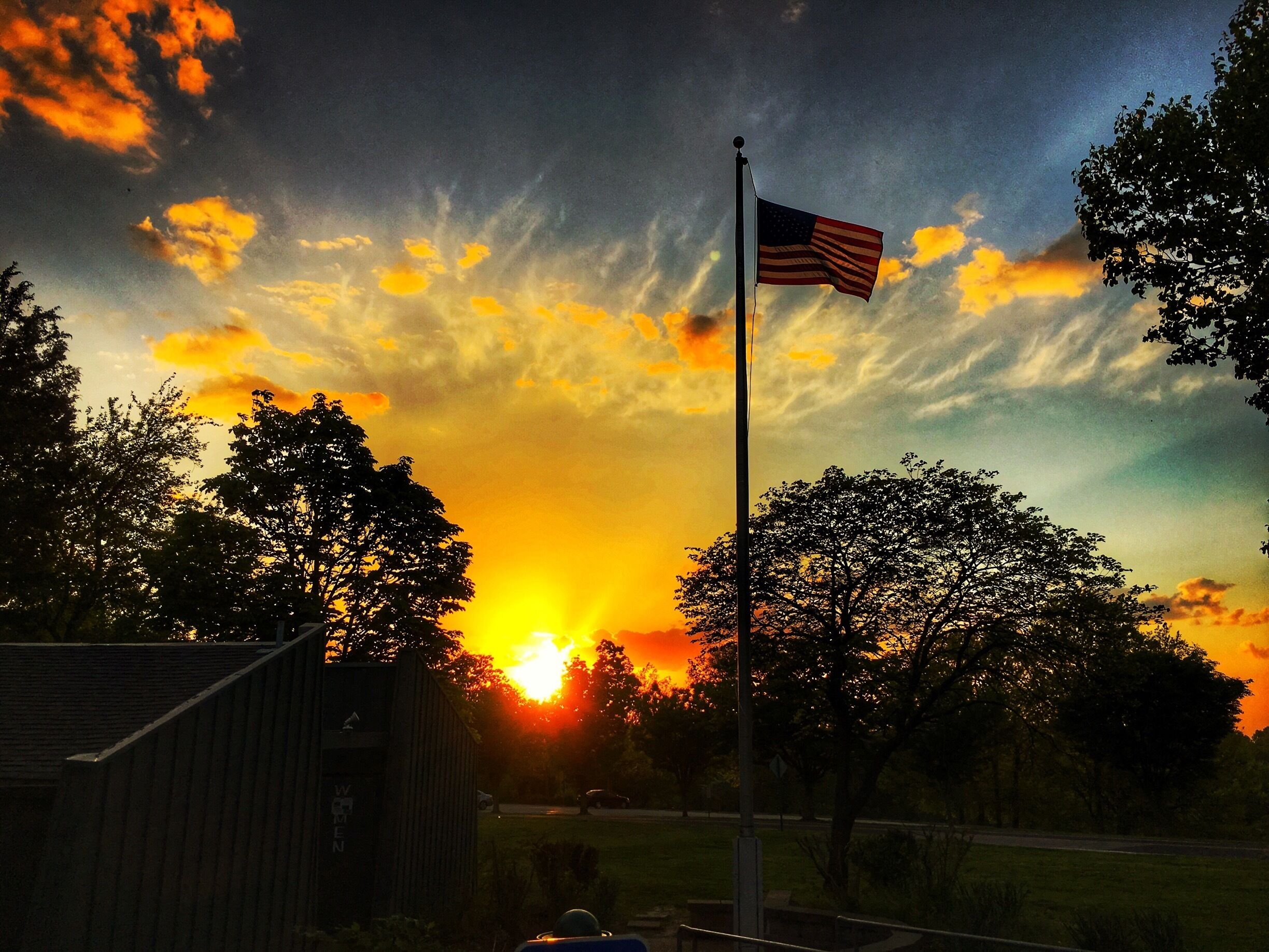 A sunset with an American flag on a flagpole, trees, and a building labeled "WOMEN".
