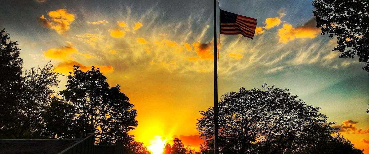 A sunset with an American flag on a flagpole, trees, and a building labeled "WOMEN".