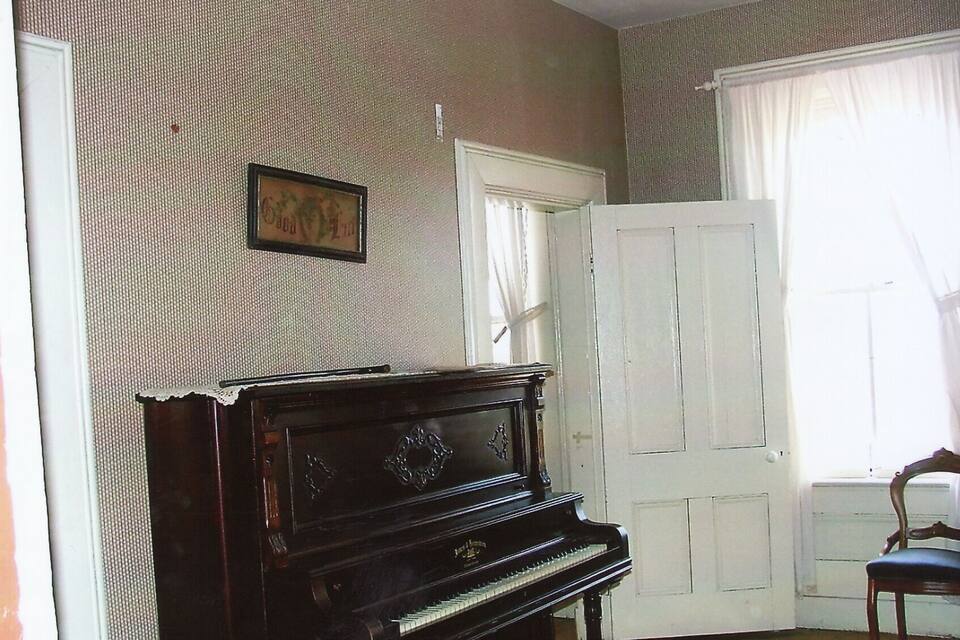 Una habitación con un piano de cola, una puerta blanca y un cuadro en la pared.