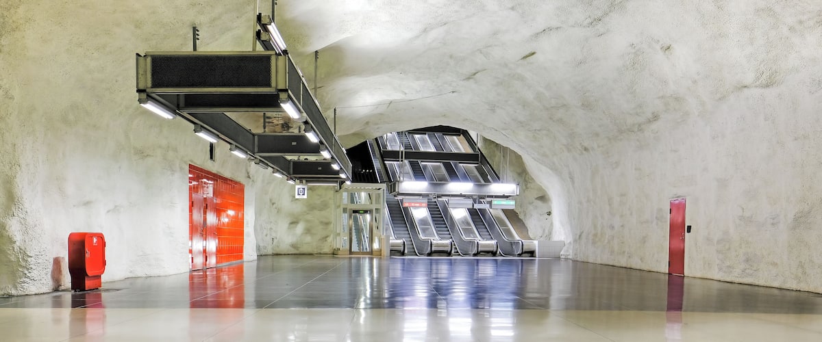 A subway station with escalators, a red emergency phone, and a tiled floor.