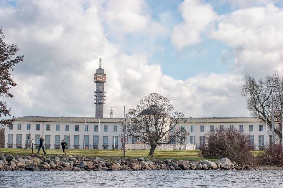 A large building with a tower, a tree, and a rocky shoreline.