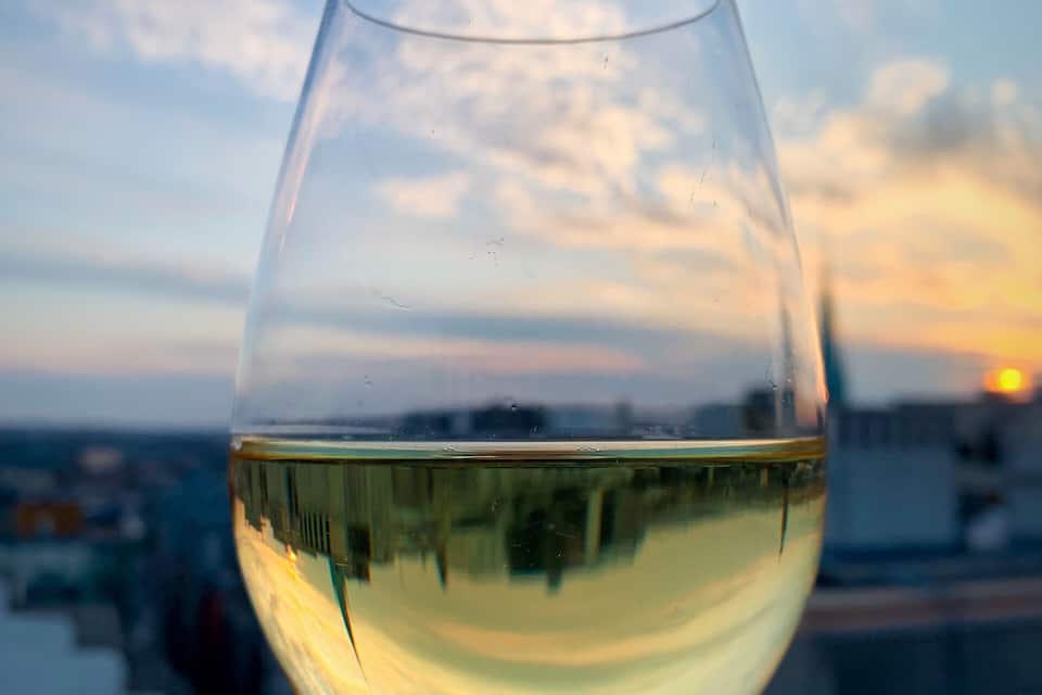 A glass of white wine held against a sunset sky.