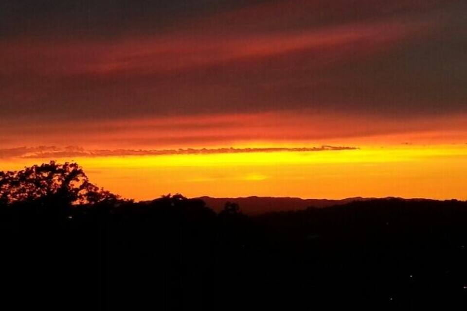 Um pôr do sol sobre uma paisagem montanhosa com árvores recortadas.