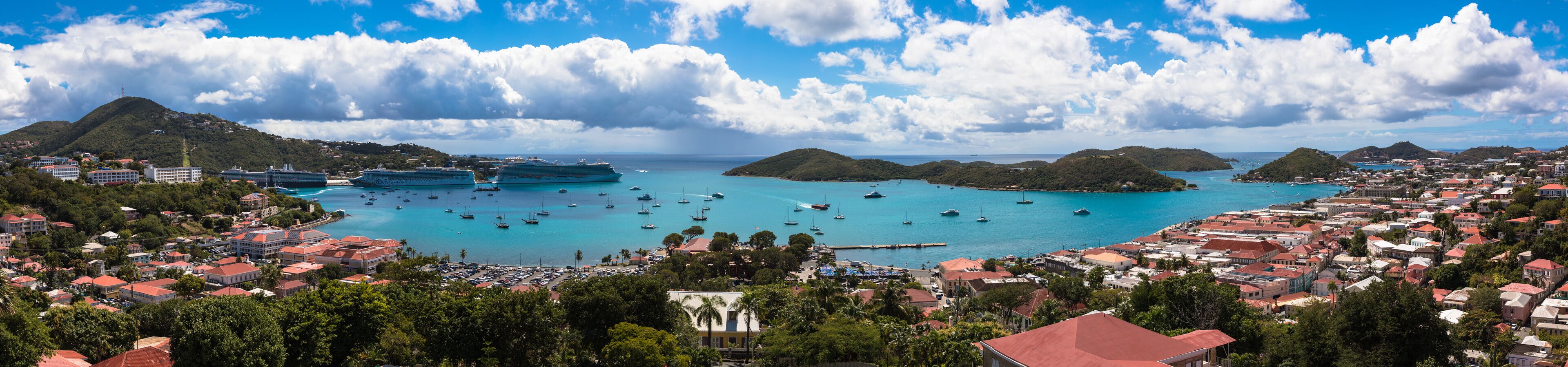 A coastal town with cruise ships docked, clear turquoise waters, and lush green hills.
