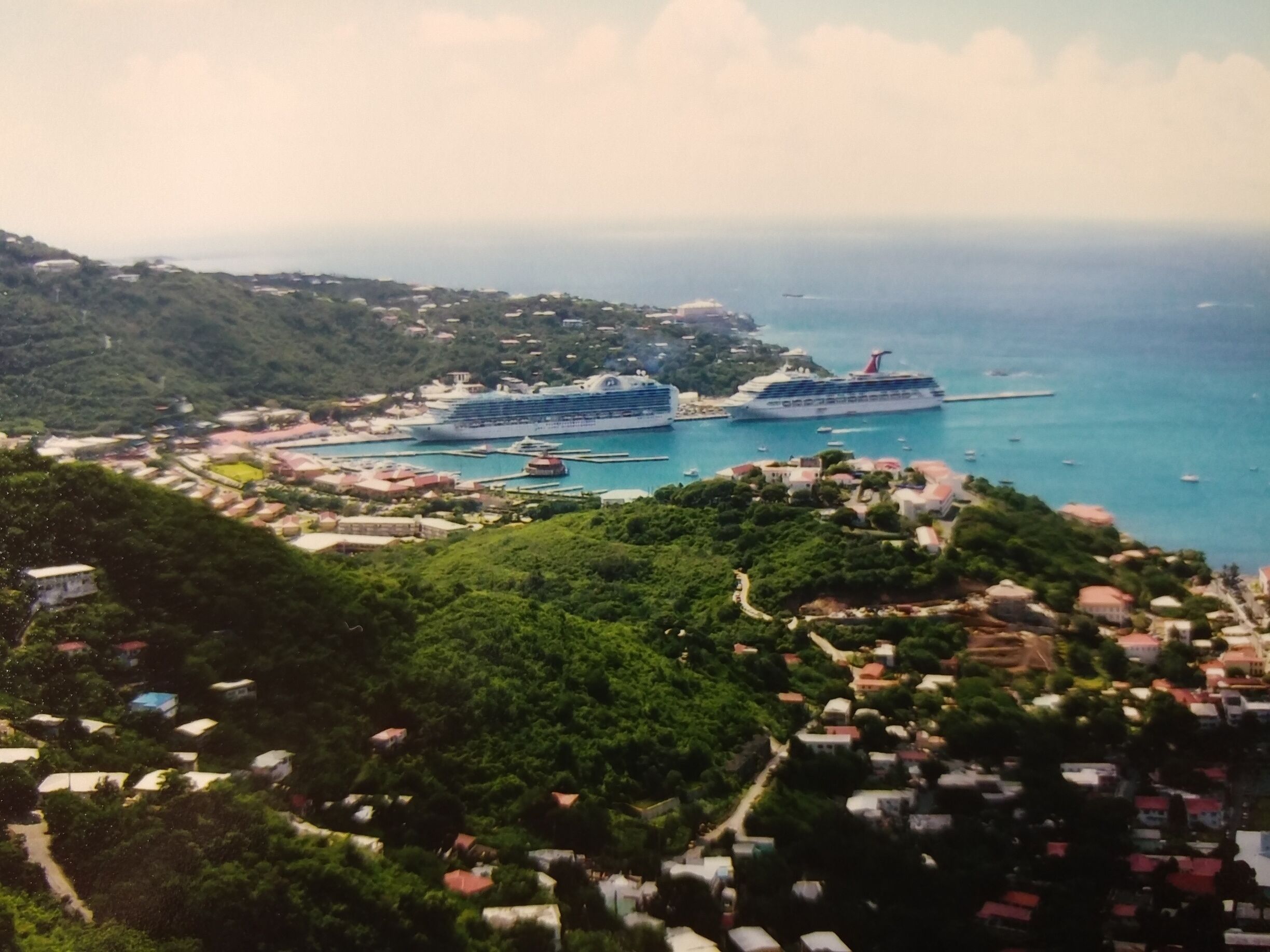 A coastal town with cruise ships docked, lush greenery, and a clear view of the sea.