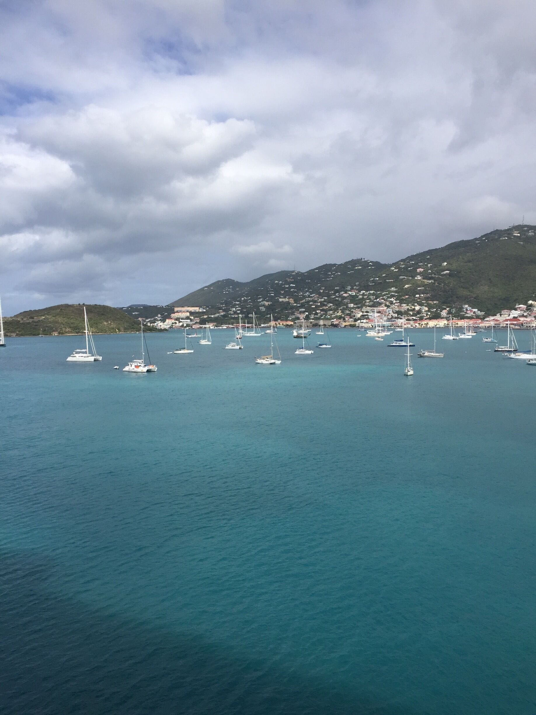 A coastal town with numerous sailboats anchored in calm turquoise waters.