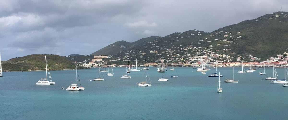 A coastal town with numerous sailboats anchored in calm turquoise waters.
