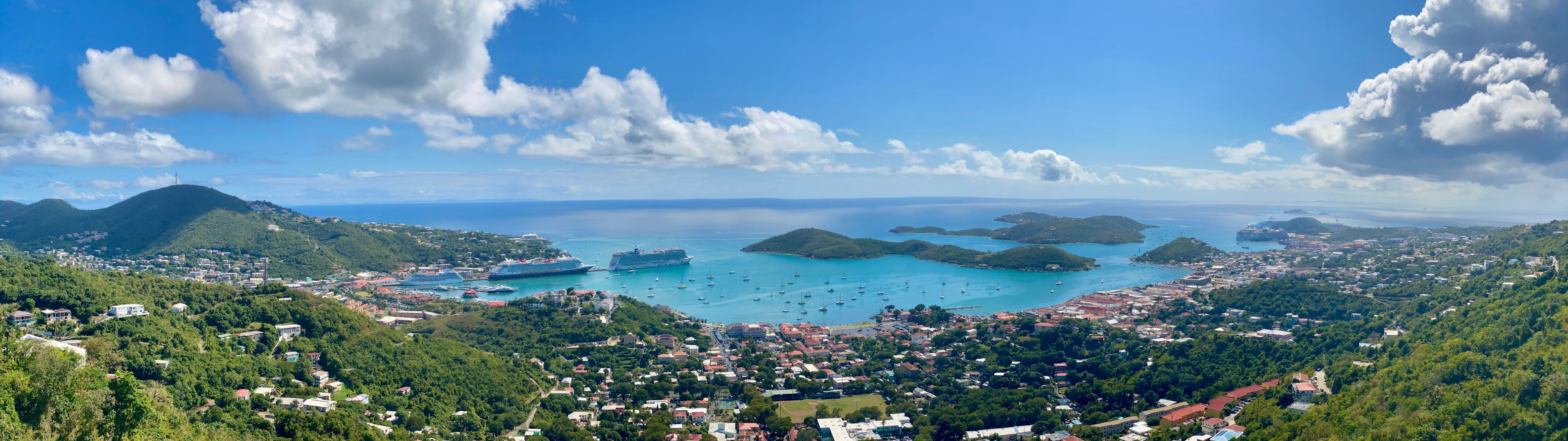 A coastal town with cruise ships, a bay with small islands, and lush green hills.