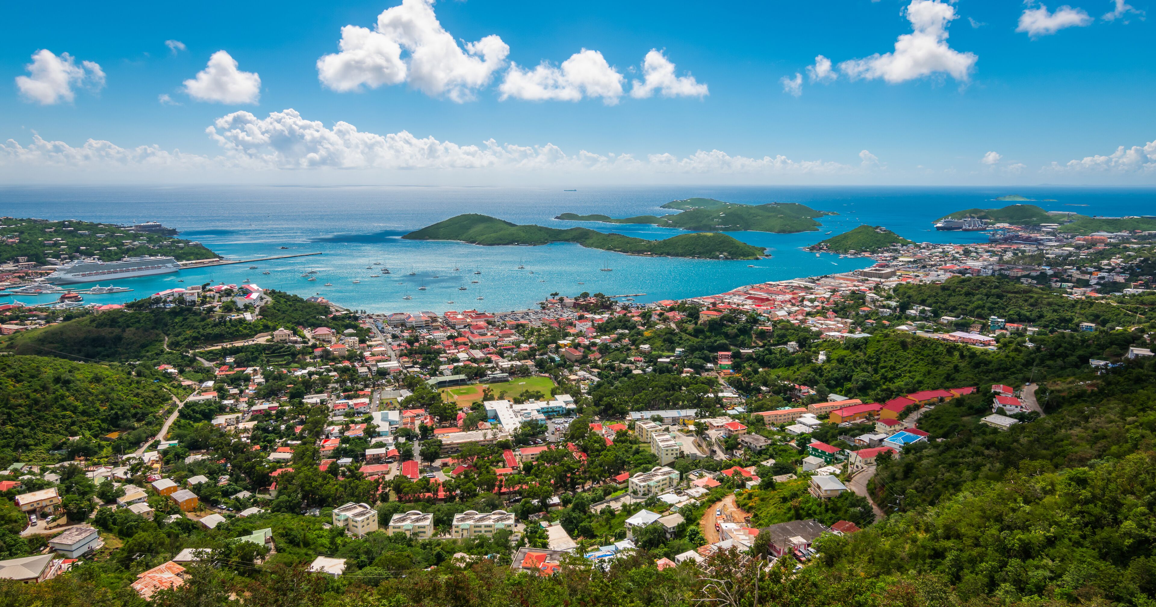 A coastal town with a marina, green hills, and a clear blue sky.