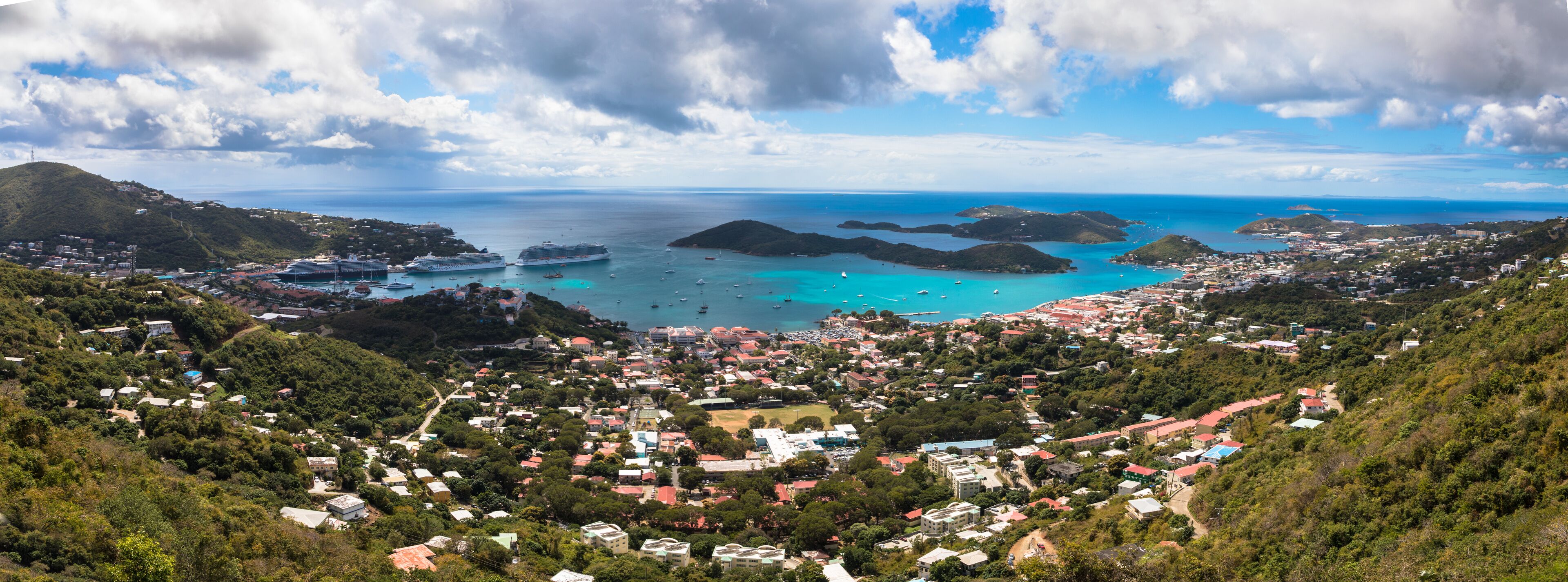 A coastal town with a harbor, cruise ships, and a mountainous backdrop.