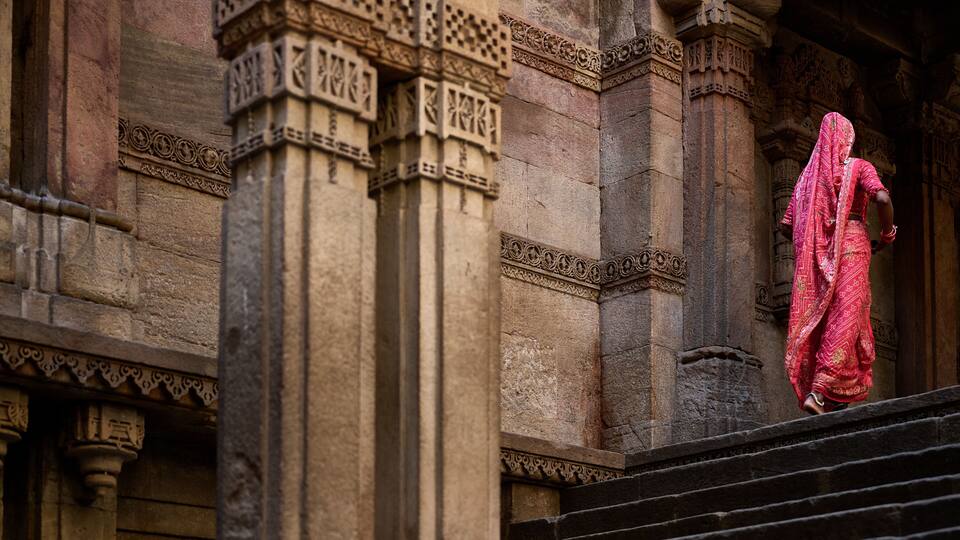 A stone building with intricate carvings and a person in traditional attire descending a set of stairs.