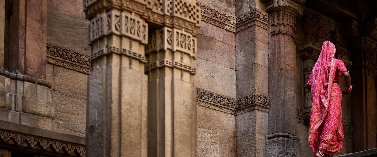 A stone building with intricate carvings and a person in traditional attire descending a set of stairs.