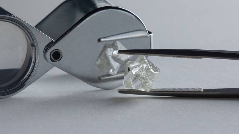 A pair of tweezers holding a clear, faceted gemstone.