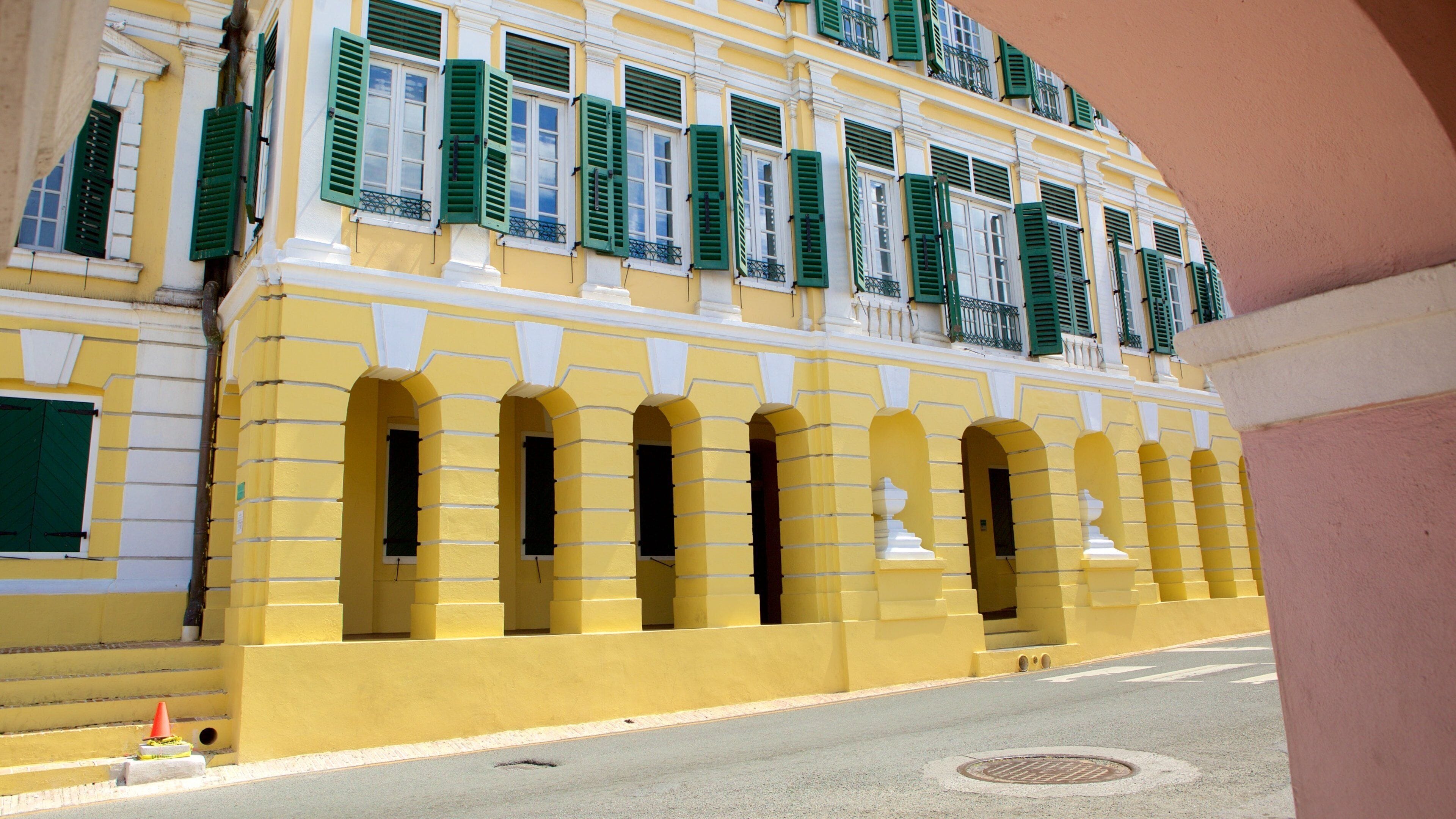 Un edificio amarillo con contraventanas verdes y detalles blancos.