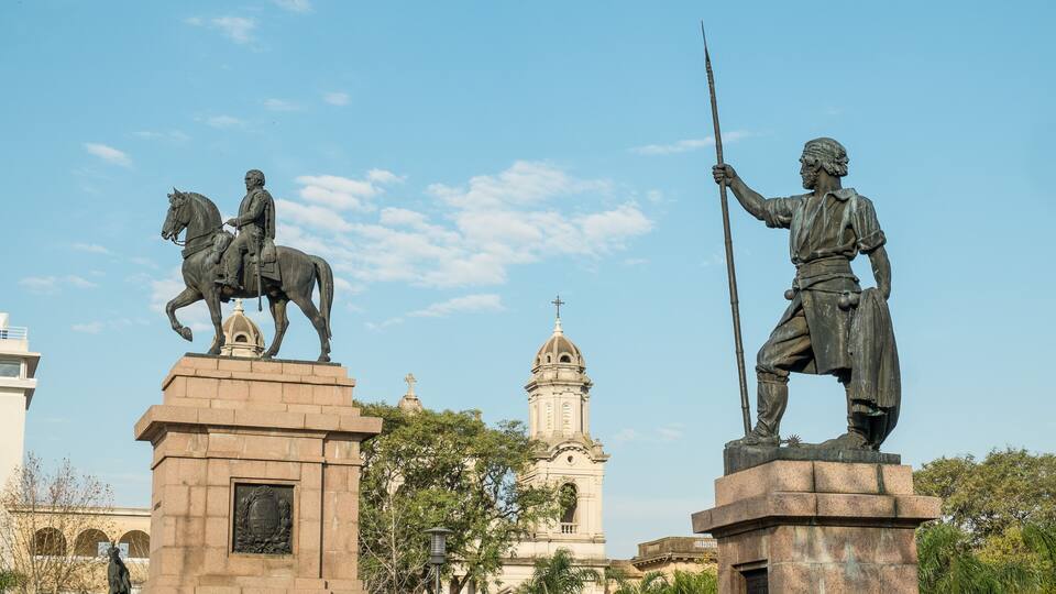 A statue of a man on horseback and another holding a spear, with a church and clear blue sky in the background.