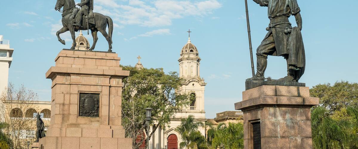 A statue of a man on horseback and another holding a spear, with a church and clear blue sky in the background.