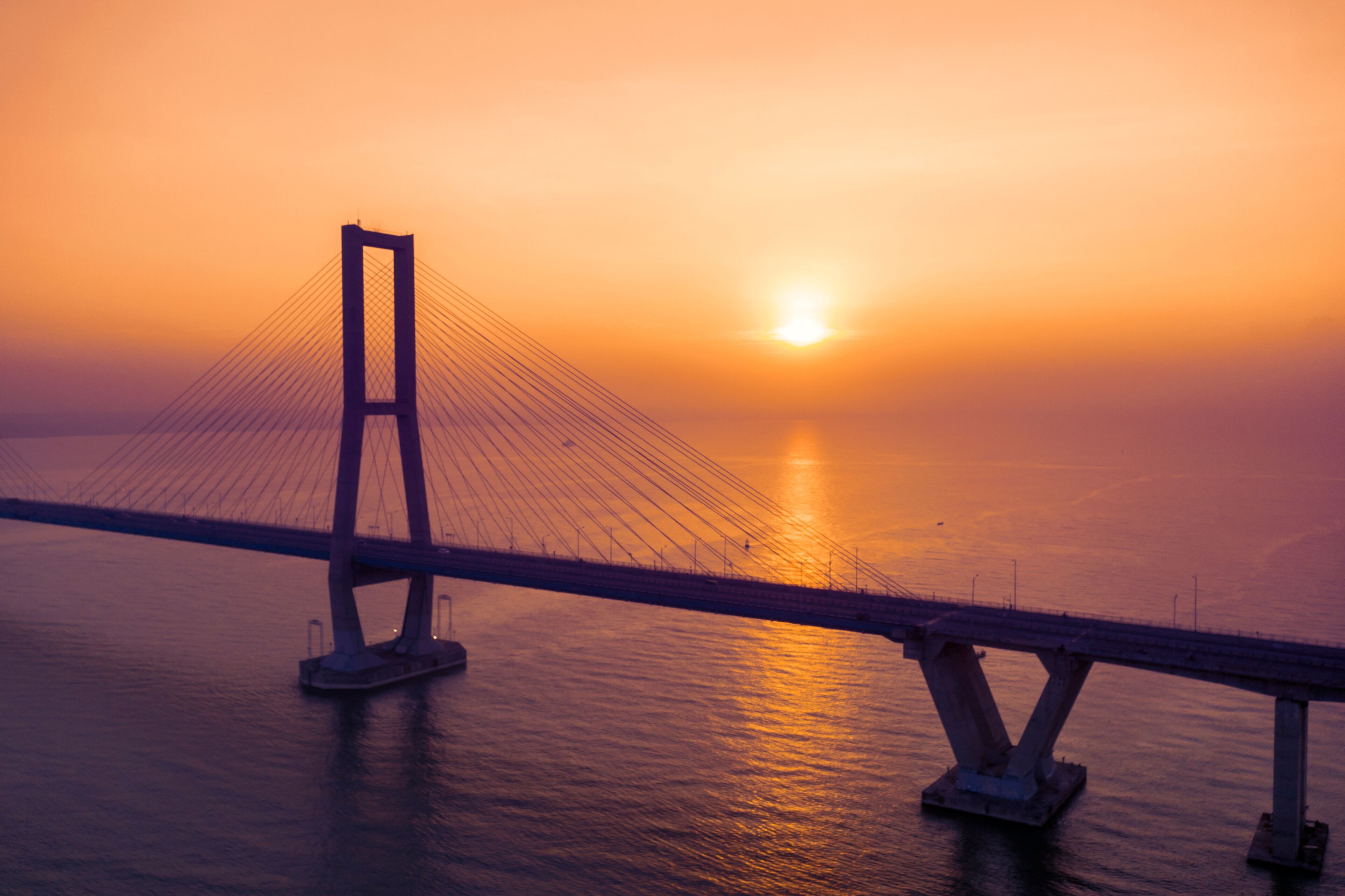 Un puente colgante al atardecer con una masa de agua tranquila debajo.