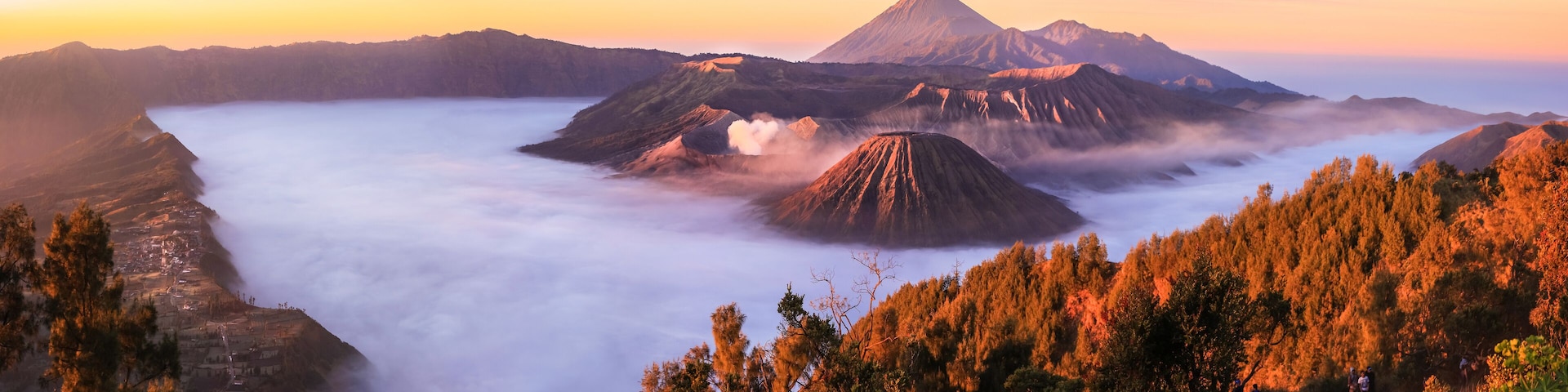 A mountain range with a prominent volcano, forested hills, and a valley shrouded in mist.