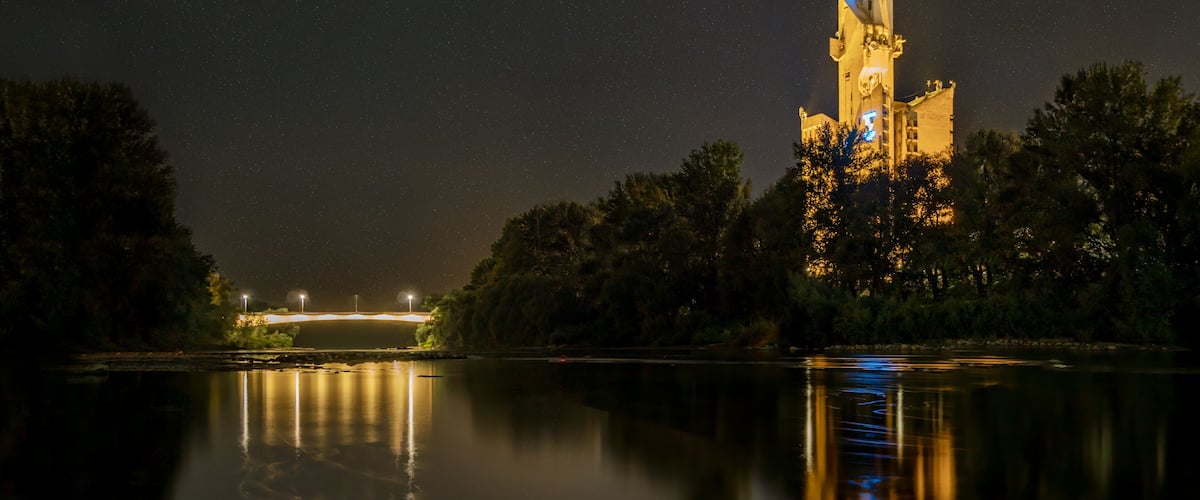 A night scene with a lit tower reflecting on a calm river.