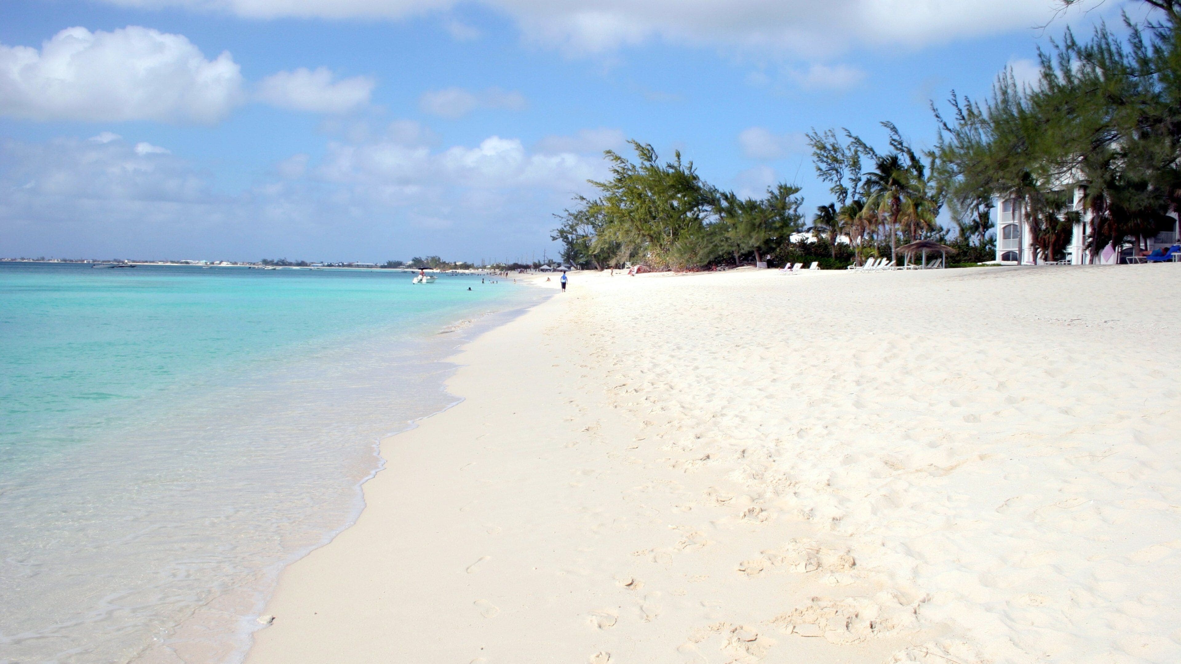 Una playa de arena con agua turquesa cristalina, palmeras y algunas personas a lo lejos.