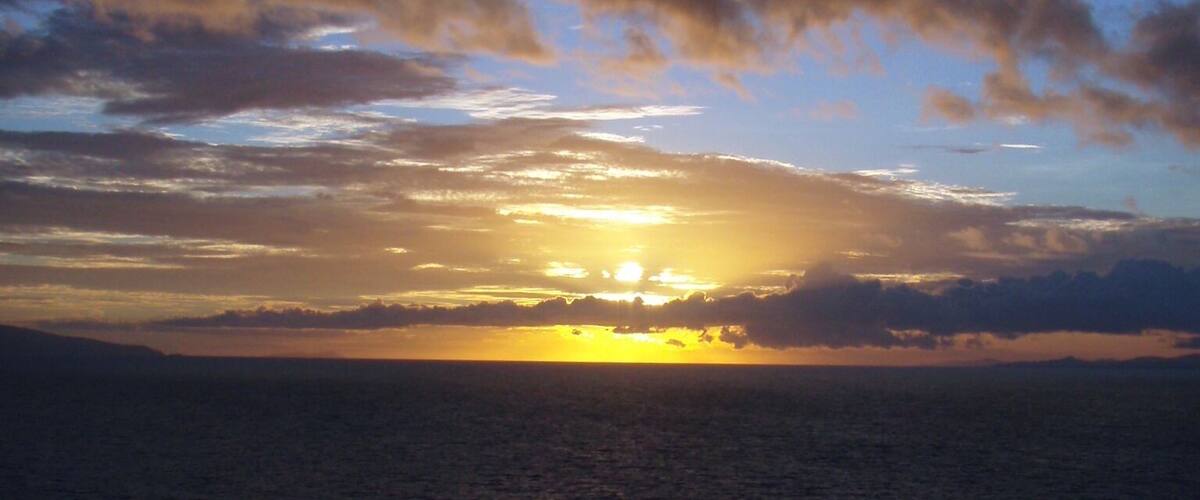 A sunset over the ocean with silhouettes of people on a dock.