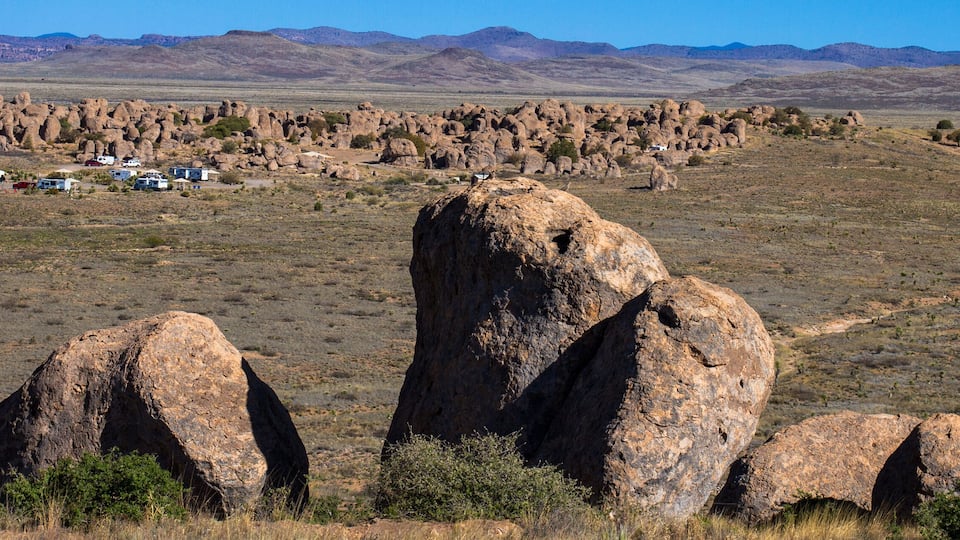 A desert landscape with prominent rock formations and a caravan park in the foreground.