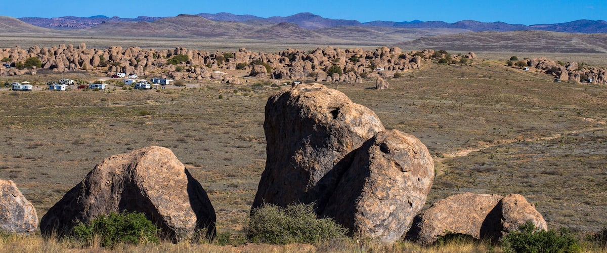 A desert landscape with prominent rock formations and a caravan park in the foreground.