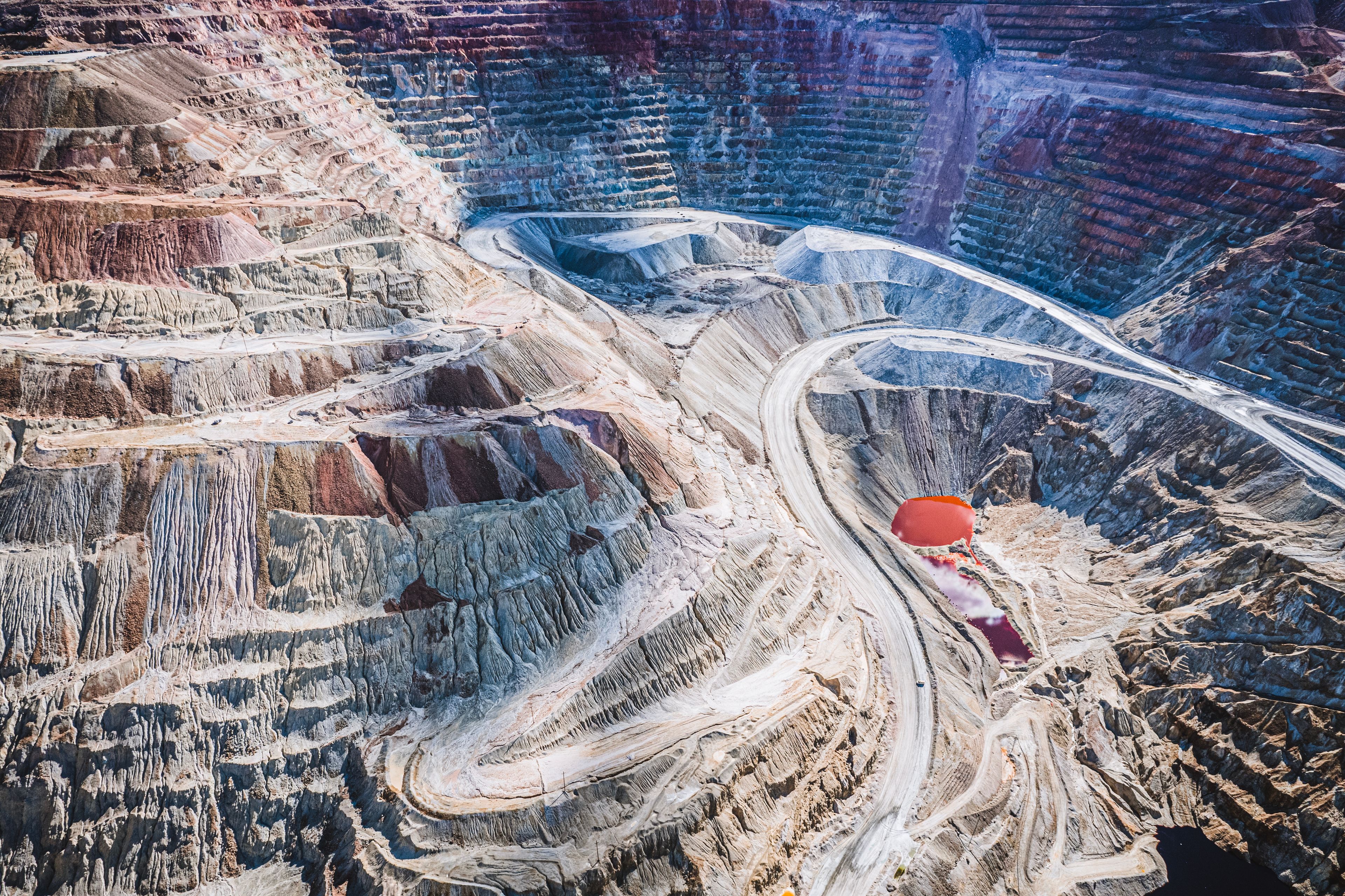 An aerial view of a large open-pit mine with winding roads and a prominent red balloon.