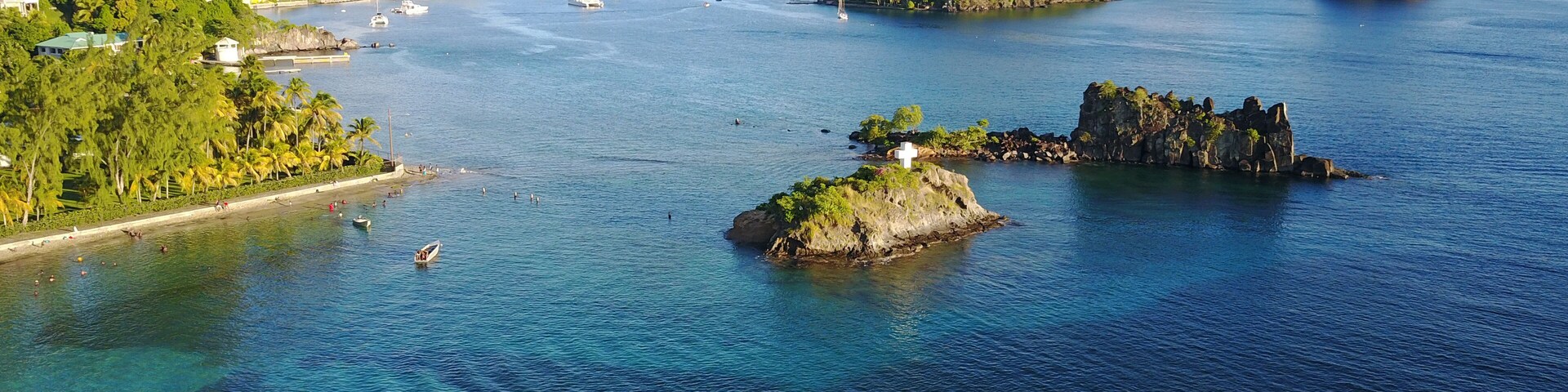 Paisagem costeira com águas azuis cristalinas, pequenas ilhas e uma linha de costa distante com edifícios.