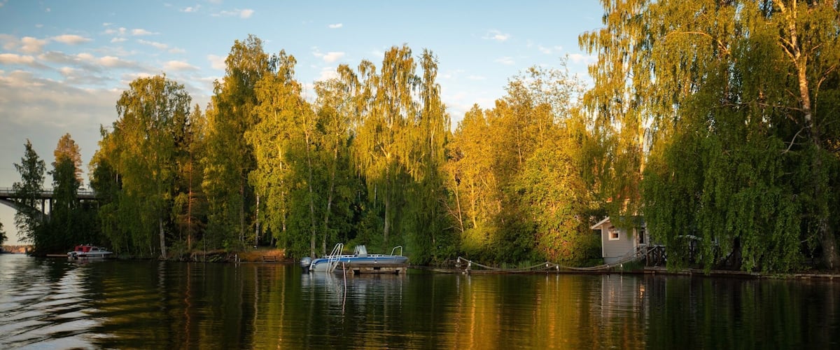 A calm lake with a small dock and a house surrounded by trees.