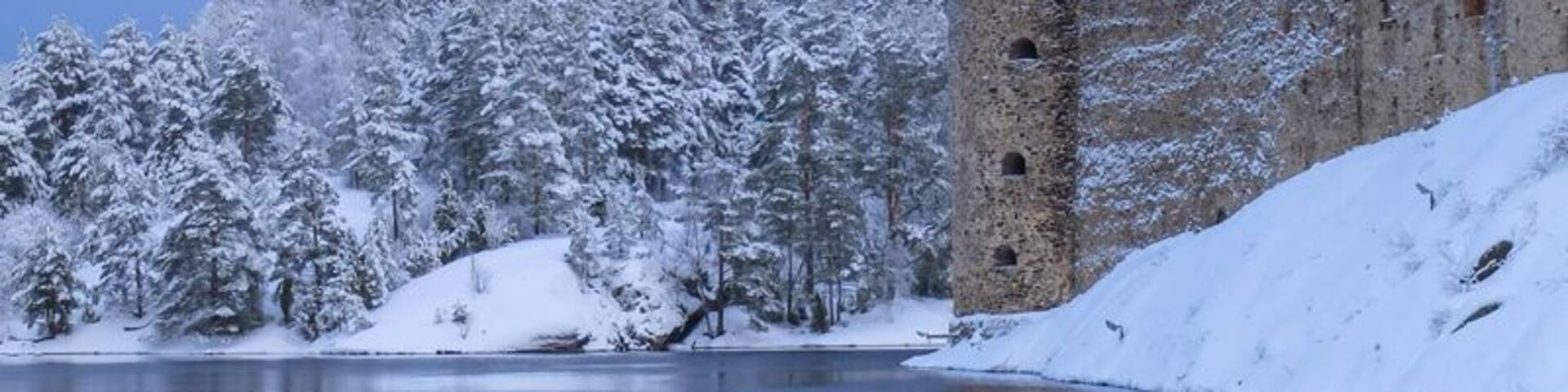 A snow-covered castle with a tower by a calm lake.