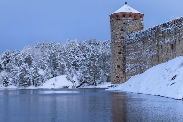 Un château enneigé, avec une tour, au bord d’un lac paisible.