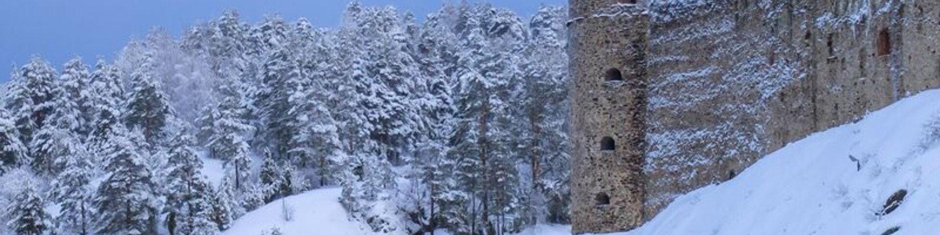 Un castillo cubierto de nieve con una torre junto a un lago tranquilo.