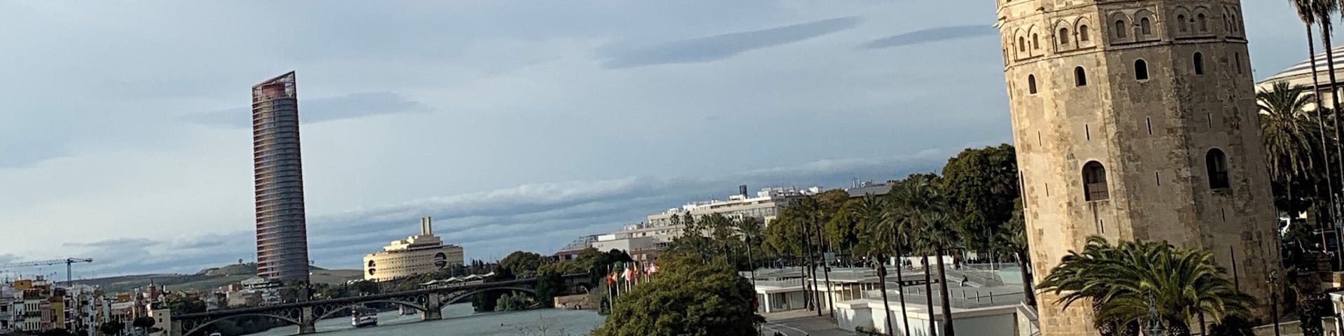 Un paseo ribereño con una torre histórica, un rascacielos moderno y un puente.