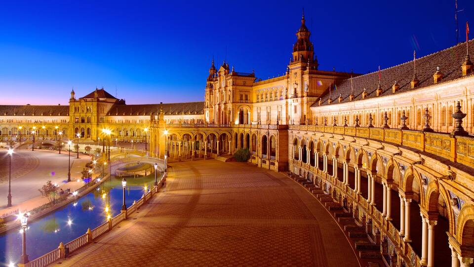 A grand, illuminated building with arched walkways and a reflective pool.