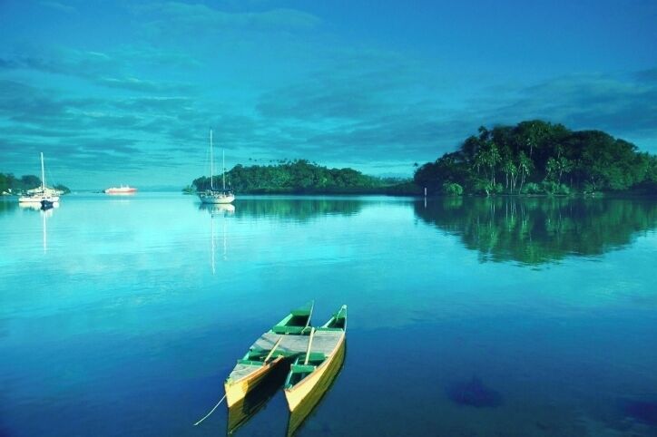 A calm lake with several boats, a small island with dense vegetation, and a clear blue sky.