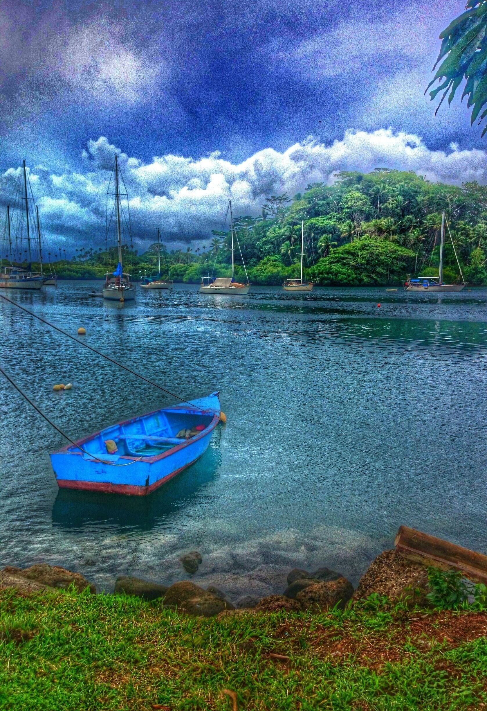 A dingy floating on the edge of Savusavu harbour, looking out over the yachts and the leafy islands just off the coast. It's a cloudy day but still bright, cooler than the last few days have been. 