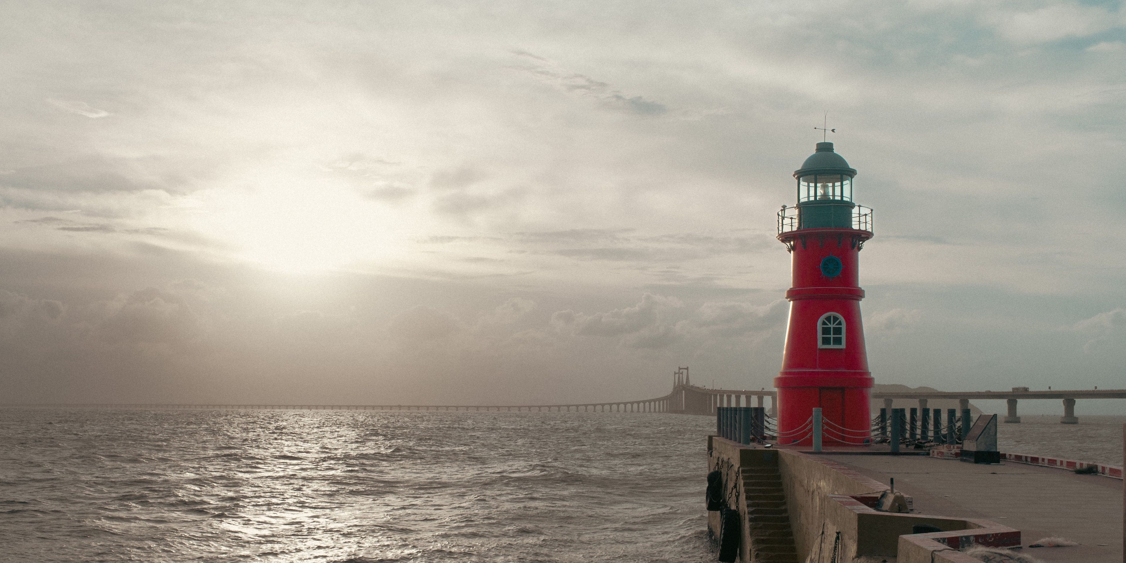 Un phare rouge au bord de la mer, sous un ciel nuageux.