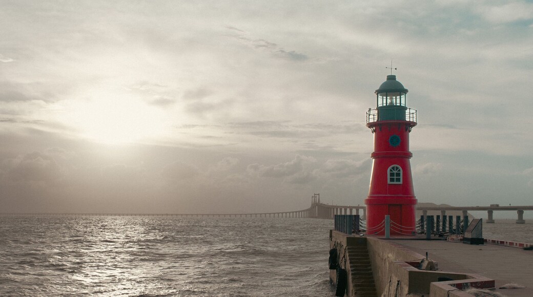 Un phare rouge au bord de la mer, sous un ciel nuageux.