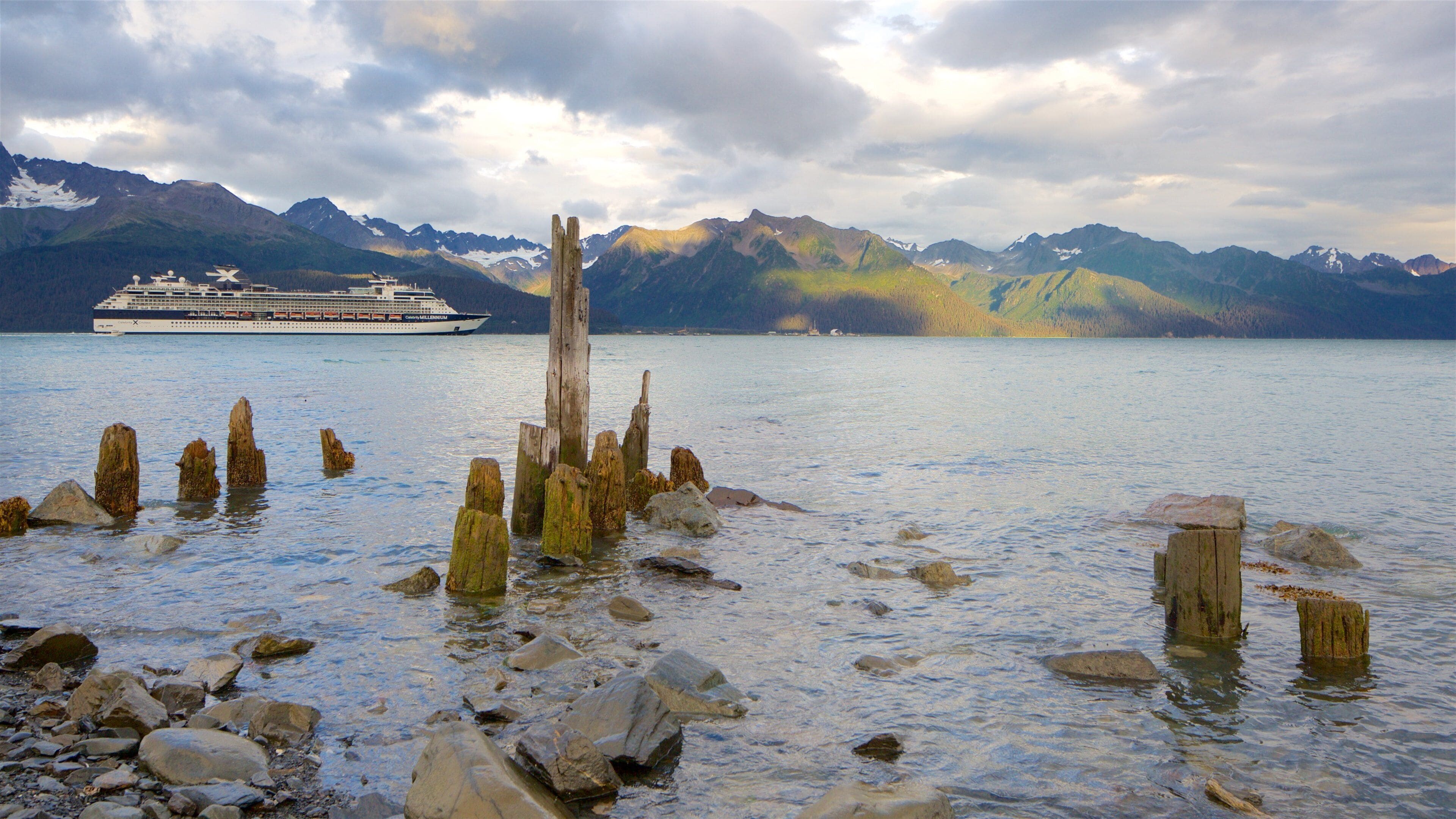 A cruise ship on a calm lake with mountains in the background and wooden posts in the foreground.