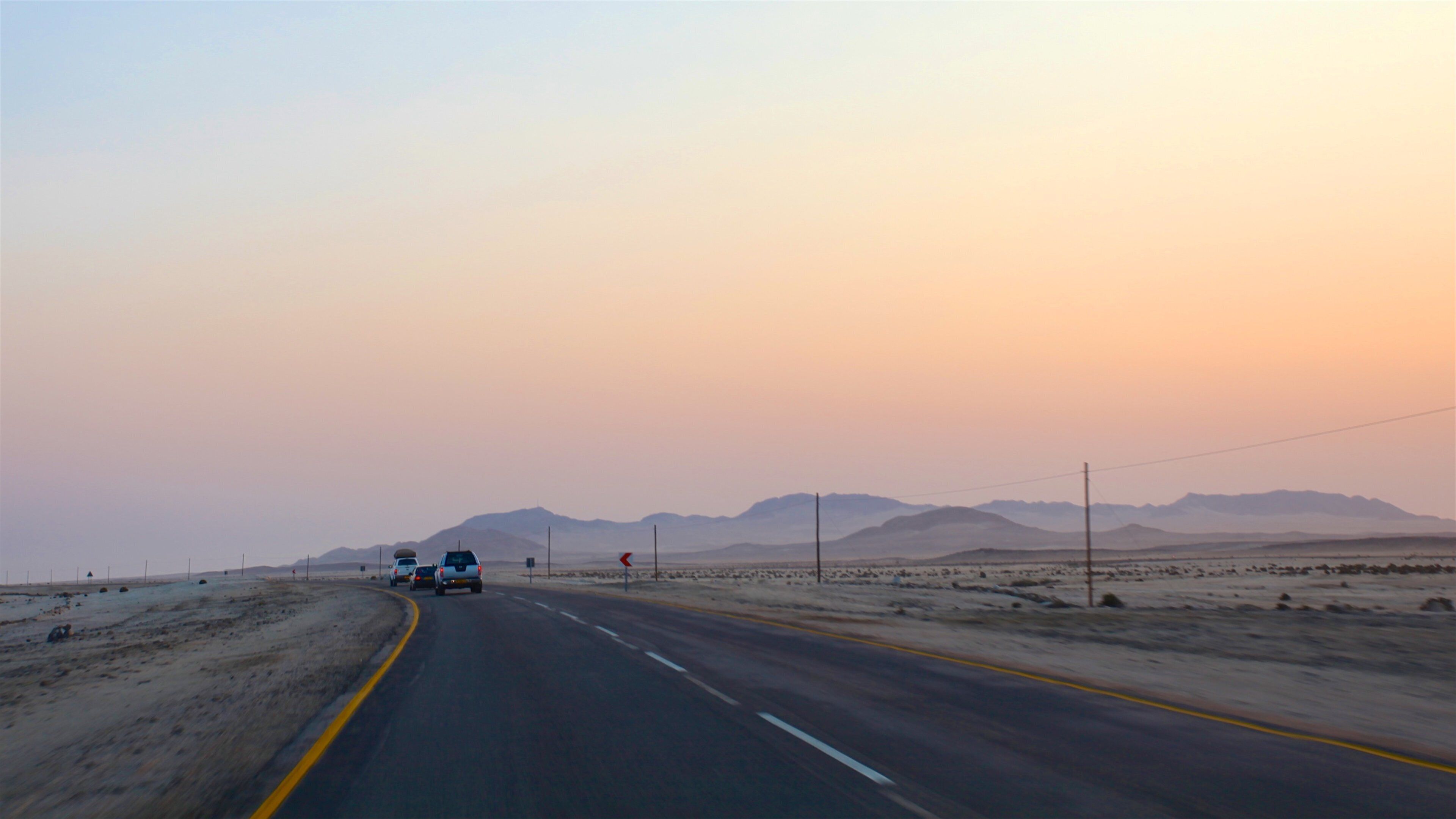 A desert road with mountains in the distance and a sunset sky.