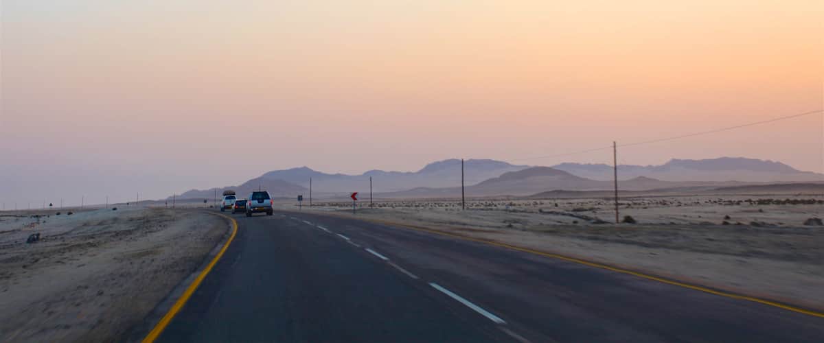 A desert road with mountains in the distance and a sunset sky.