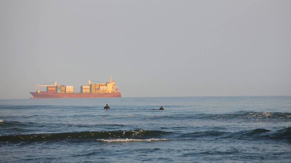 A large cargo ship on the ocean with two people swimming in the water.