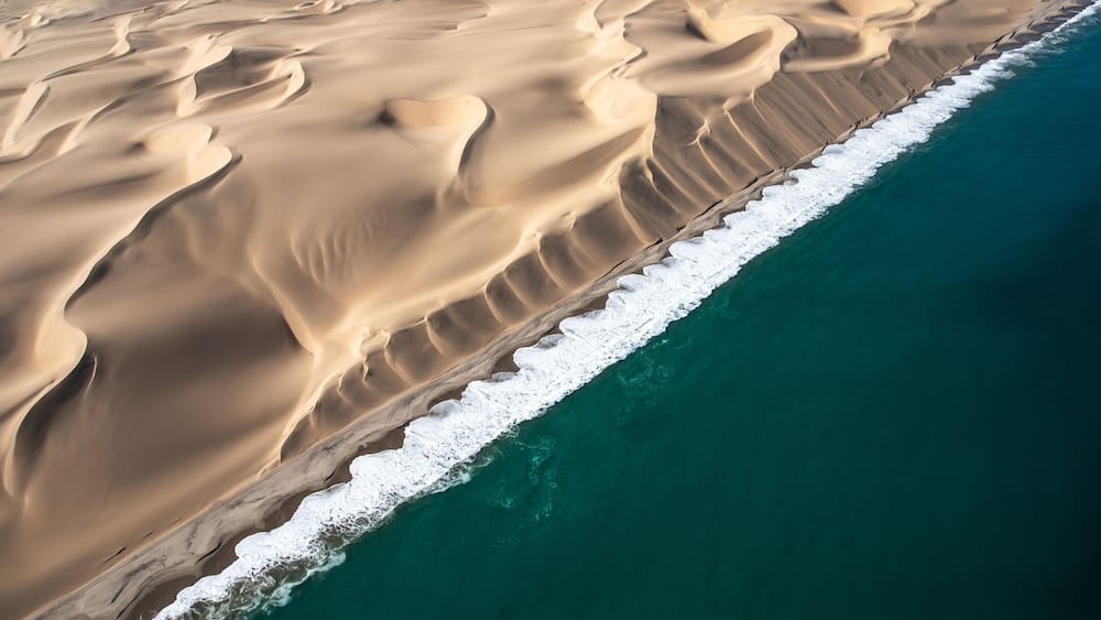 Weite Wüstenlandschaft mit Sanddünen und einer Küstenlinie.