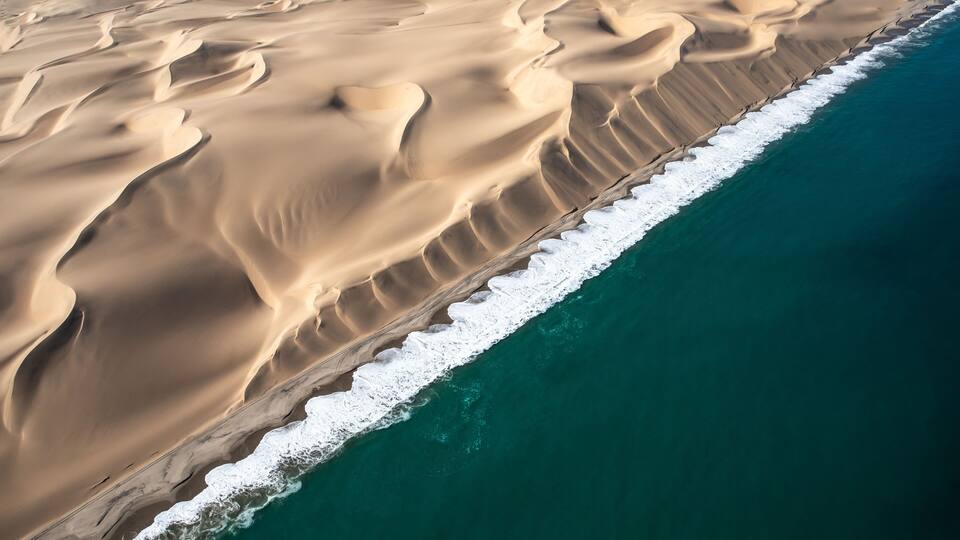 A vast desert landscape with sand dunes and a coastline.